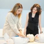 Two women learning CPR techniques on training mannequins during a healthcare workshop.